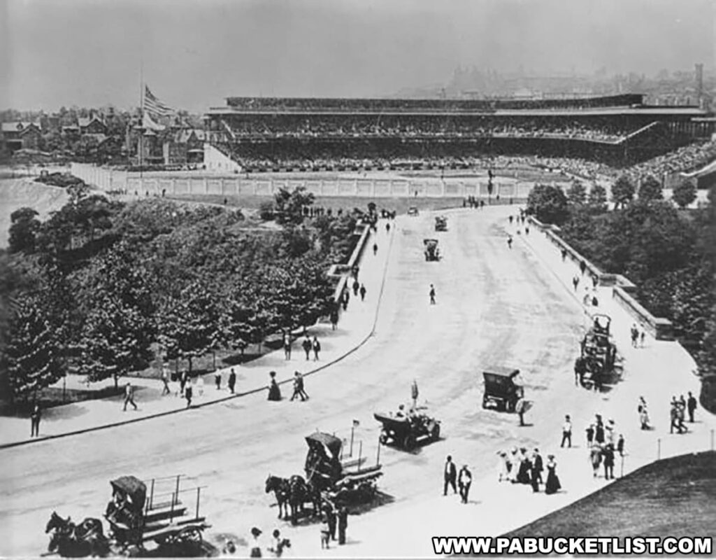 An early 20th-century black and white photograph of Forbes Field in the Oakland neighborhood of Pittsburgh. The image showcases the ballpark bustling with spectators, highlighted by the grandstands packed with fans. In the foreground, an expansive, tree-lined boulevard leads to the stadium, bustling with pedestrians and vintage automobiles, some drawn by horses. The scene captures a moment in time, reflecting the early days of the automobile era, with the attire of the individuals and the design of the vehicles anchoring the image in history. The stadium, surrounded by residential houses, is the focal point of community and baseball history as the home of the Pittsburgh Pirates.