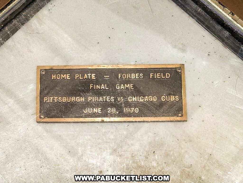 A commemorative plaque embedded in the floor marks the original location of home plate from Forbes Field in Pittsburgh. The brass plaque reads "HOME PLATE — FORBES FIELD FINAL GAME PITTSBURGH PIRATES vs CHICAGO CUBS JUNE 28, 1970," honoring the last baseball game played at the historic park. The plaque serves as a memorial to the rich history of the Pirates and their former stadium, set against the concrete ground, a reminder of the sports heritage that once graced the Oakland neighborhood.