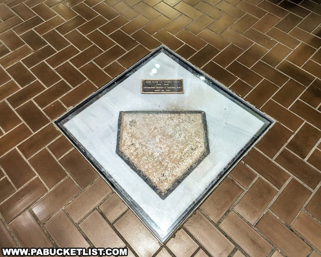 Encased in a protective glass cover set into a tiled floor is the original home plate from Forbes Field. Above it, a small plaque commemorates the final game played at the historic ballpark, listing the Pittsburgh Pirates against the Chicago Cubs on June 28, 1970. The home plate, a weathered pentagon of white rubber, is preserved as a poignant relic, symbolizing the countless games and sports history that unfolded in the Oakland neighborhood of Pittsburgh where Forbes Field once stood as a temple of baseball for the Pittsburgh Pirates.
