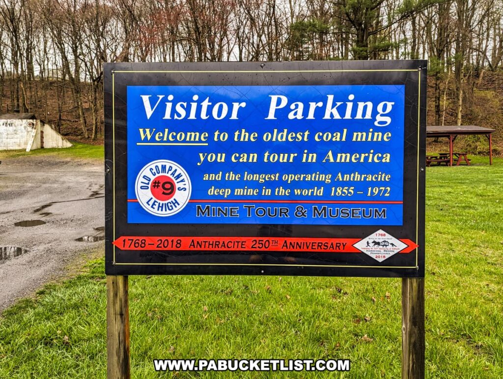 A sign at the Number 9 Coal Mine and Museum in Carbon County, PA, reading "Visitor Parking." The sign welcomes visitors to "the oldest coal mine you can tour in America and the longest operating Anthracite deep mine in the world 1855 – 1972." The Old Company's Lehigh logo is featured, along with a mention of the "Anthracite 250th Anniversary." The sign is positioned on a grassy area with trees in the background and a picnic table nearby, suggesting a tranquil area for visitors to gather.