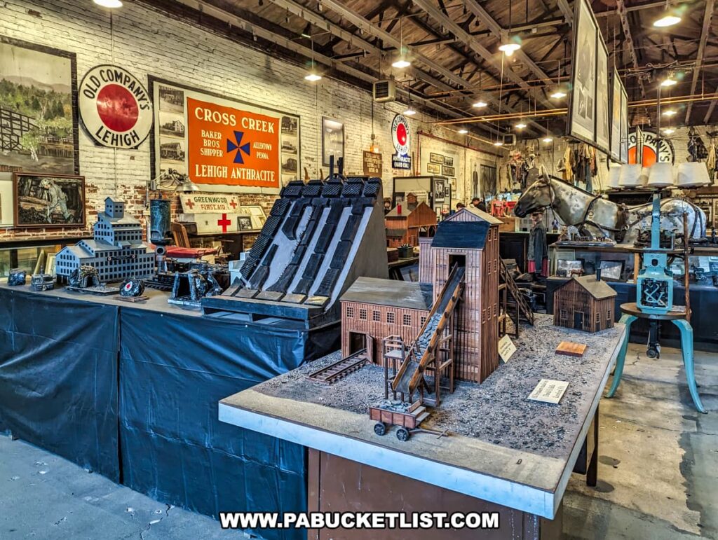 The interior of the Number 9 Coal Mine and Museum features a scale model of an anthracite coal breaker, displaying the intricate architecture and operational components of coal processing. The exhibit is complemented by various mining tools, equipment, and historical photographs in the background, including large signs such as "OLD COMPANY'S LEHIGH" and "CROSS CREEK" with symbols of mining heritage. The museum's high wooden ceilings and brick walls create an authentic and rustic atmosphere that pays homage to the coal mining industry.