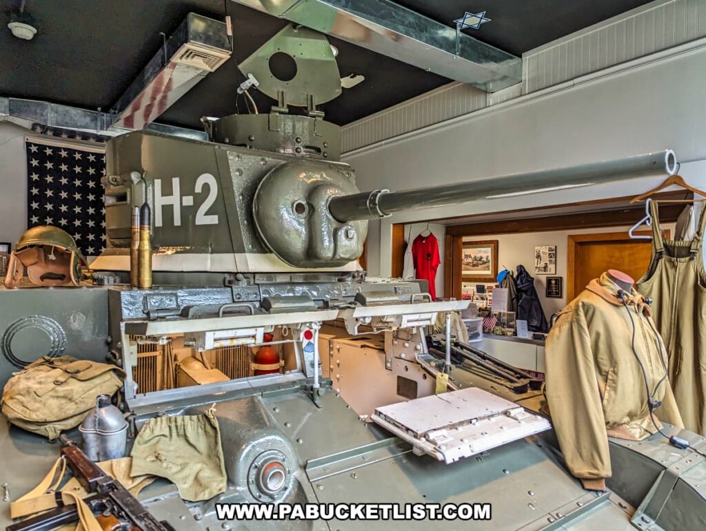An exhibit at the Stuart Tank Museum in Berwick, Pennsylvania, showcasing a front view of an M3 Stuart Light Tank marked with "H-2," displayed with military gear, an American flag backdrop, and museum artifacts including a rifle, helmet, and informational posters.