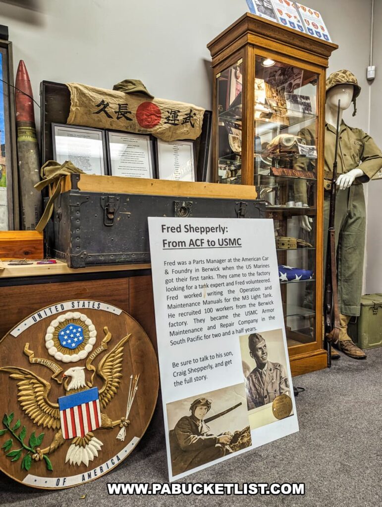 An exhibit at the Stuart Tank Museum in Berwick, Pennsylvania, featuring memorabilia related to Fred Shepperly, a Parts Manager at the American Car & Foundry, including a mannequin in military uniform, a Japanese flag, an informational poster with Fred's photo, and a wooden plaque with the Great Seal of the United States.