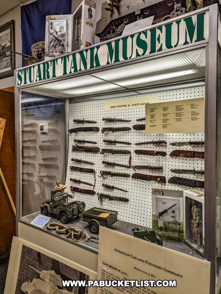 An exhibit at the Stuart Tank Museum in Berwick, Pennsylvania, showcasing a collection of WWII fighting and utility knives on display, accompanied by miniature models of military vehicles and informative signage from the American Car and Foundry Company.