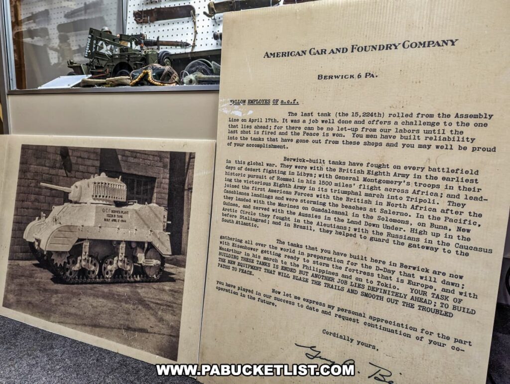 A display at the Stuart Tank Museum in Berwick, Pennsylvania, featuring a historical letter from the American Car and Foundry Company, a black and white photograph of a Stuart tank, and a small model of a tank and equipment, commemorating the production and significance of the tanks built there during WWII.