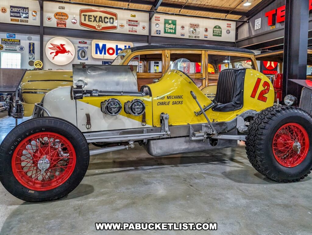 A 1930s sprint car on display at Barry's Car Barn in Lancaster County, Pennsylvania. The car features a white and yellow body with the number 12 painted in red, and 'Chief Mechanic Charlie Sacks' written on the side. The vintage vehicle is showcased in front of a backdrop filled with classic automotive signage from brands like Texaco, Mobil, and Goodyear, evoking a nostalgic atmosphere of mid-20th century American automobile culture.
