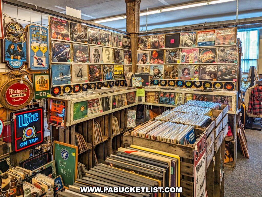 A well-organized vinyl record section at the Burning Bridge Antiques Market in Lancaster County, PA. The display features walls lined with album covers from various genres and artists, along with shelves holding crates filled with vinyl records. Neon beer signs and vintage advertisements adorn the walls, adding a retro ambiance to the space. The records are categorized and labeled for easy browsing, showcasing a wide variety of music for collectors and enthusiasts. This section highlights the diverse offerings of the market, which features over 200 vendors in its expansive, three-story space.