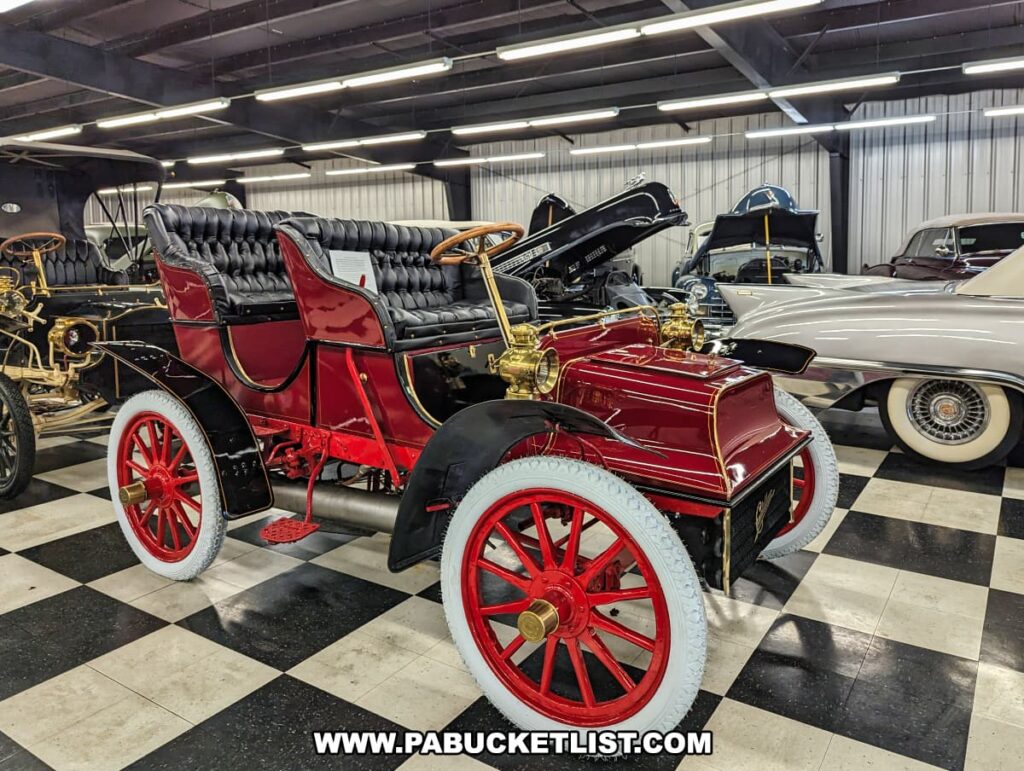 A beautifully restored 1906 Model K Cadillac with a rich red exterior and intricate brass details on display at the Greenberg Cadillac Museum. The car features elegant black leather seating and white tires, exemplifying the meticulous restoration efforts that bring these historic vehicles back to life. Other vintage Cadillacs are visible in the background, showcasing the extensive collection at the museum.