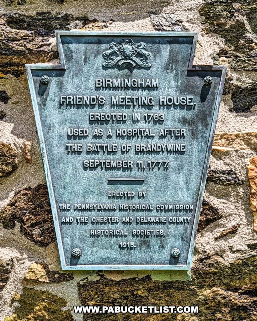 Plaque on the Birmingham Friends Meeting House at Brandywine Battlefield Park in Chester County, Pennsylvania. The plaque notes the building was erected in 1763 and used as a hospital after the Battle of Brandywine on September 11, 1777. The plaque was erected by the Pennsylvania Historical Commission and the Chester and Delaware County Historical Societies in 1915. The plaque is set against a stone wall, reflecting the building's historical significance.