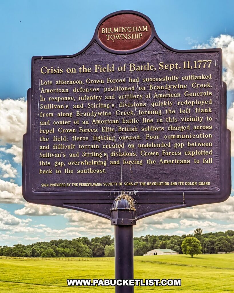 Historical marker at Birmingham Hill in Brandywine Battlefield Park, Chester County, Pennsylvania, describing the events of September 11, 1777. The marker details how Crown Forces outflanked American defenses along Brandywine Creek, leading to fierce fighting and poor communication among American divisions. The British exploited the gap, overwhelming American forces and forcing them to retreat. The marker is provided by the Pennsylvania Society of Sons of the Revolution and its Color Guard. The background shows a grassy field with a split-rail fence and a clear blue sky.