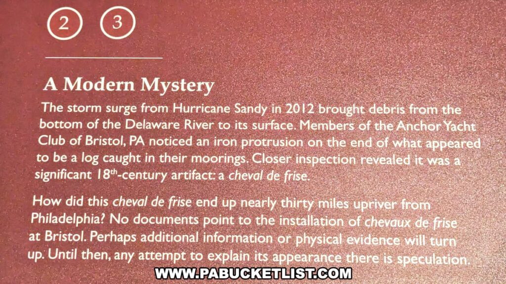 An informational sign at Brandywine Battlefield Park in Chester County, Pennsylvania, titled "A Modern Mystery," describes the discovery of an 18th-century artifact called a cheval de frise. The artifact was found after Hurricane Sandy in 2012 brought debris from the bottom of the Delaware River to the surface. Members of the Anchor Yacht Club of Bristol, PA, noticed an iron protrusion on what appeared to be a log caught in their moorings. Upon closer inspection, it was identified as a significant 18th-century artifact. The sign poses the question of how the cheval de frise ended up nearly thirty miles upriver from Philadelphia, noting that no documents indicate its installation at Bristol, and inviting speculation until further evidence is found.