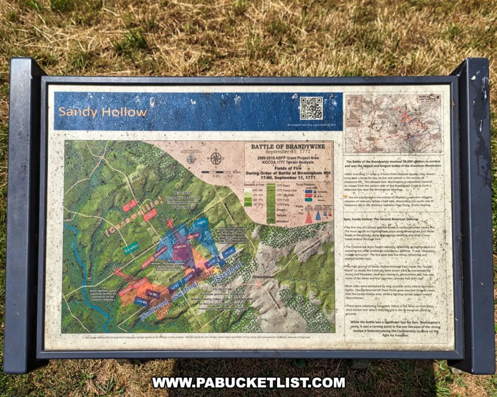 An interpretive sign at Sandy Hollow in Brandywine Battlefield Park, Chester County, Pennsylvania, provides detailed information about the Battle of Brandywine on September 11, 1777. The sign includes a map showing troop movements and key locations during the battle, highlighting areas such as Birmingham Hill and Osborne Hill. Text on the right side of the sign explains the significance of the battle, noting that it involved 26,000 soldiers and was one of the largest battles of the American Revolution. The sign is mounted on a stand and situated on a grassy area, offering historical insights to visitors.