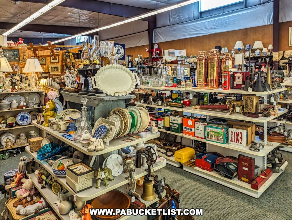 A section of Cackleberry Farm Antique Mall in Lancaster County, PA, featuring a wide variety of vintage glassware, ceramics, and collectibles. Shelves are filled with items such as elegant glass decanters, plates, lamps, and various decorative pieces. The display also includes antique fire extinguishers, tins, and other eclectic items, showcasing the diverse selection available. The well-organized and brightly lit space invites visitors to explore and discover unique treasures from different eras.