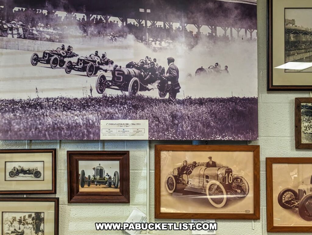 A display of vintage racing photographs at the Eastern Museum of Motor Racing in Adams County, Pennsylvania. The centerpiece is a large, historic photo of the 1st Indianapolis 500 in May 1911, capturing early race cars in action on the track. Surrounding it are framed photos of classic race cars and drivers, each depicting significant moments in motor racing history. The exhibit showcases the evolution of racing, with images of early 20th-century vehicles and events, reflecting the museum's mission to preserve and interpret the rich heritage of American motor racing, particularly in Pennsylvania and the surrounding regions.