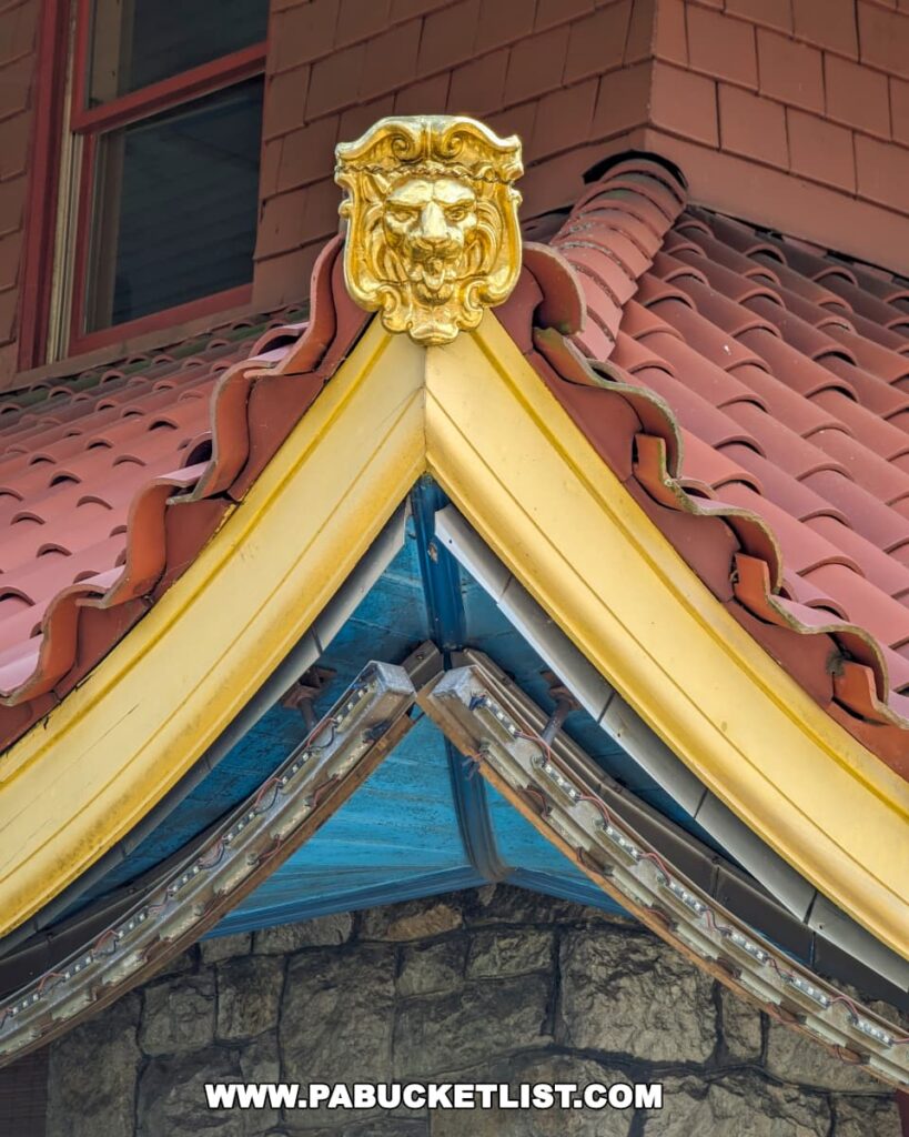 The photo showcases a close-up of the intricate architectural details of the Reading Pagoda in Berks County, PA. It highlights the ornate gold lionhead ornamentation at the corner of the upswept red-tiled roof. The craftsmanship of the stonework and the wooden trim is also visible, emphasizing the Pagoda's exotic revival architectural style.