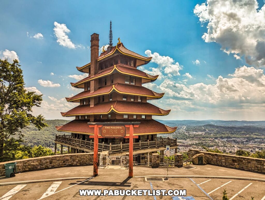 The image captures the majestic Reading Pagoda in Berks County, PA, standing tall with its seven stories and five overhanging red roofs. The torii gate at the entrance adds an authentic oriental touch. The Pagoda is set against a backdrop of rolling hills and a vibrant blue sky with scattered clouds, offering a panoramic view of the city of Reading below.