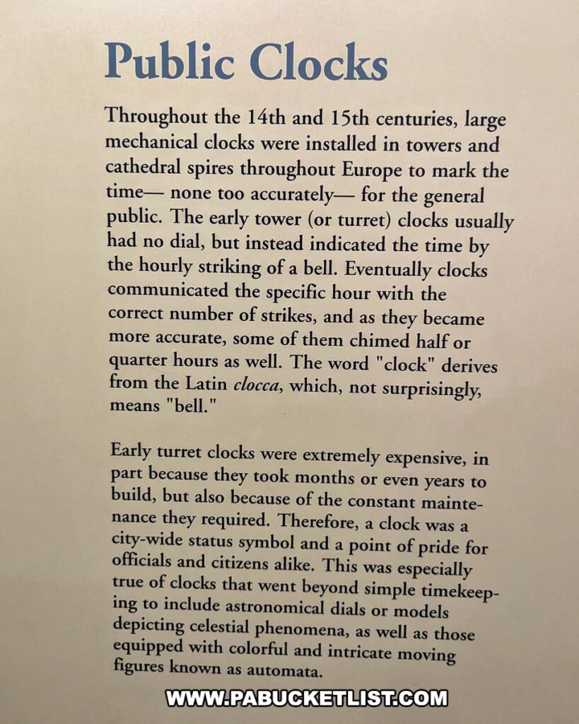 An informational display at the National Watch and Clock Museum in Lancaster County, Pennsylvania, titled "Public Clocks." The text explains the history of large mechanical clocks installed in towers and cathedral spires throughout Europe during the 14th and 15th centuries. These early tower clocks, which often lacked dials, indicated time by the hourly striking of a bell. As technology advanced, these clocks became more accurate and began chiming the specific hour, and sometimes half or quarter hours, with the correct number of strikes. The display notes that the word "clock" derives from the Latin "clocca," meaning "bell." It also discusses the significance and expense of early turret clocks, which took months or years to build and required constant maintenance, making them city-wide status symbols and points of pride. Some advanced clocks included astronomical dials or models depicting celestial phenomena and featured colorful, intricate moving figures known as automata.