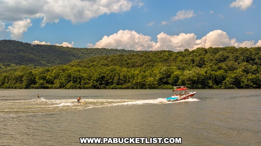 A vibrant scene on Raystown Lake with a motorboat towing two water skiers. The skiers cut through the wake, creating splashes and waves. The lush green hills and a bright blue sky with fluffy white clouds provide a picturesque backdrop for this lively recreational activity.