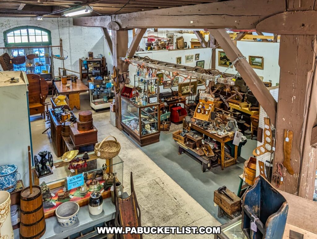 An overhead view of the main floor inside Rollermills Antique Marketplace in Lewisburg, PA, showcasing wooden beams from the historic 1880s flour mill and vendor booths filled with antique furniture, glassware, vintage decor, and unique collectibles, all arranged in a spacious and well-lit shopping environment.