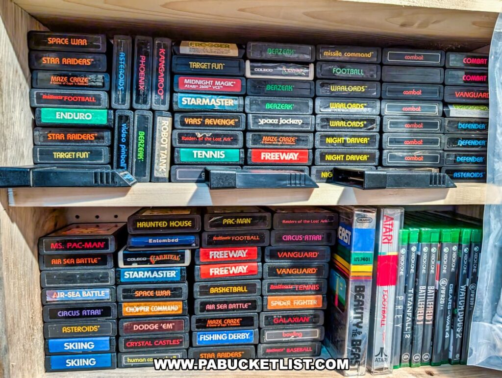 A shelf inside Rollermills Antique Marketplace in Lewisburg, PA, displaying a collection of vintage Atari 2600 game cartridges, including classics like *Ms. Pac-Man*, *Asteroids*, *Space War*, and *Defender*, alongside a selection of Xbox games, showcasing the marketplace’s variety of retro gaming collectibles.