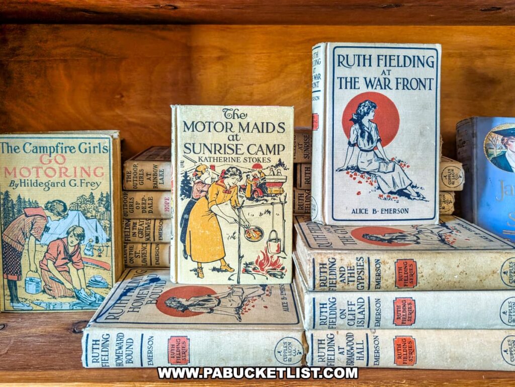 A wooden shelf inside Rollermills Antique Marketplace in Lewisburg, PA, displaying a collection of vintage hardcover books, including early 20th-century titles such as The Motor Maids at Sunrise Camp, Ruth Fielding at the War Front, and The Campfire Girls Go Motoring, featuring beautifully illustrated covers and classic storytelling.