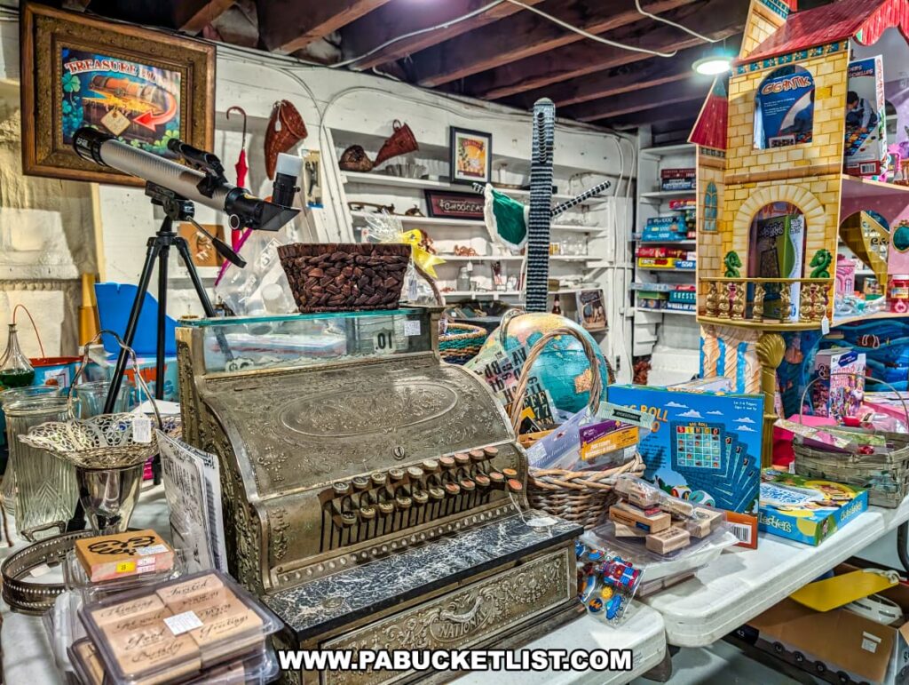 A vendor booth inside Rollermills Antique Marketplace in Lewisburg, PA, featuring a vintage ornate cash register, a telescope, a globe, classic board games, collectible toys, and decorative antiques, all displayed under exposed wooden beams in the historic 1880s flour mill.