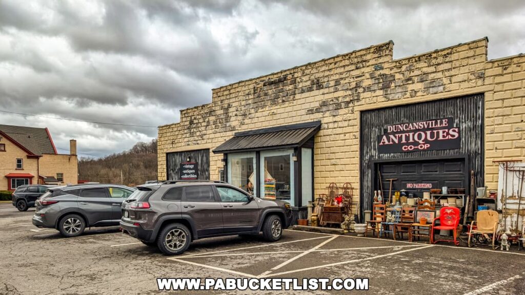 Exterior view of the Duncansville Antiques Co-Op in Blair County, Pennsylvania, showing the storefront of the multi-vendor antiques and collectibles store with vintage items displayed outside and vehicles parked in front under cloudy skies.