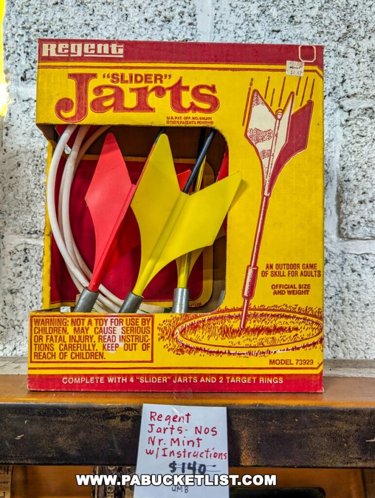 Vintage Regent "Slider" Jarts lawn dart set on display at the Duncansville Antiques Co-Op in Blair County, Pennsylvania, featuring its original packaging with bold red and yellow graphics, warning labels, and a handwritten price tag noting the set as near mint with instructions.