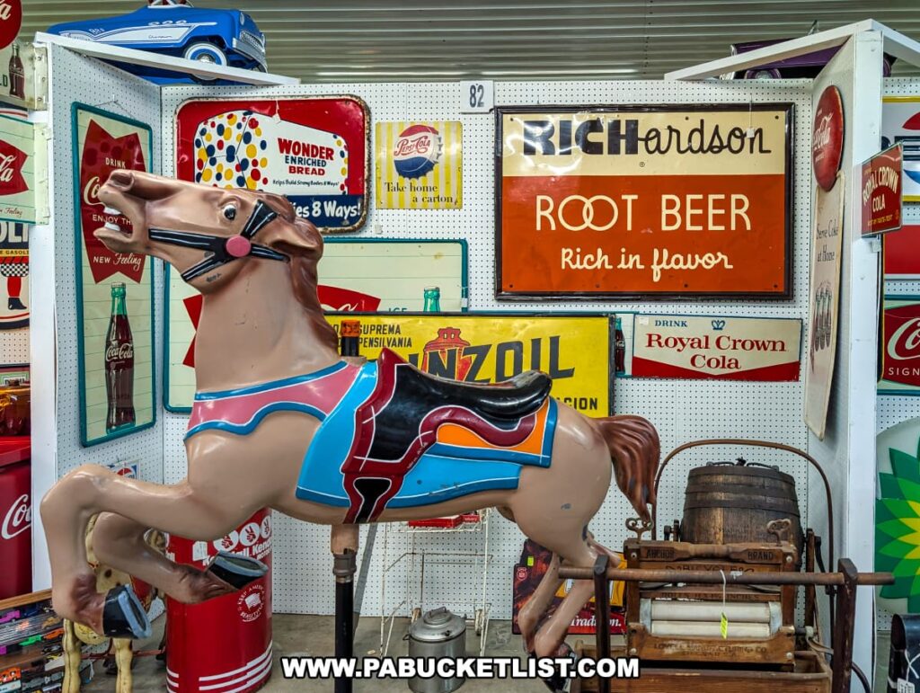 Vendor booth at the Lewisburg Antique Malls in Union County, Pennsylvania, featuring a vintage carousel horse prominently displayed alongside colorful antique advertising signs, including Richardson Root Beer, Coca-Cola, Royal Crown Cola, and Wonder Bread.