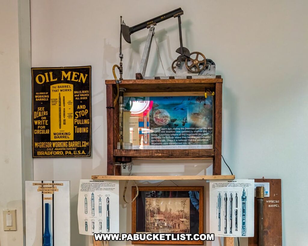 Interactive exhibit at the Penn Brad Oil Museum in McKean County, Pennsylvania, featuring a small working model of an oil pump jack atop a display cabinet showing an educational video about oil drilling; surrounding the exhibit are diagrams and advertisements for McGregor Working Barrel Company from Bradford, PA, highlighting tools and equipment used in the oil industry, with vintage illustrations and technical drawings explaining the function of working barrels and other oil field tools.