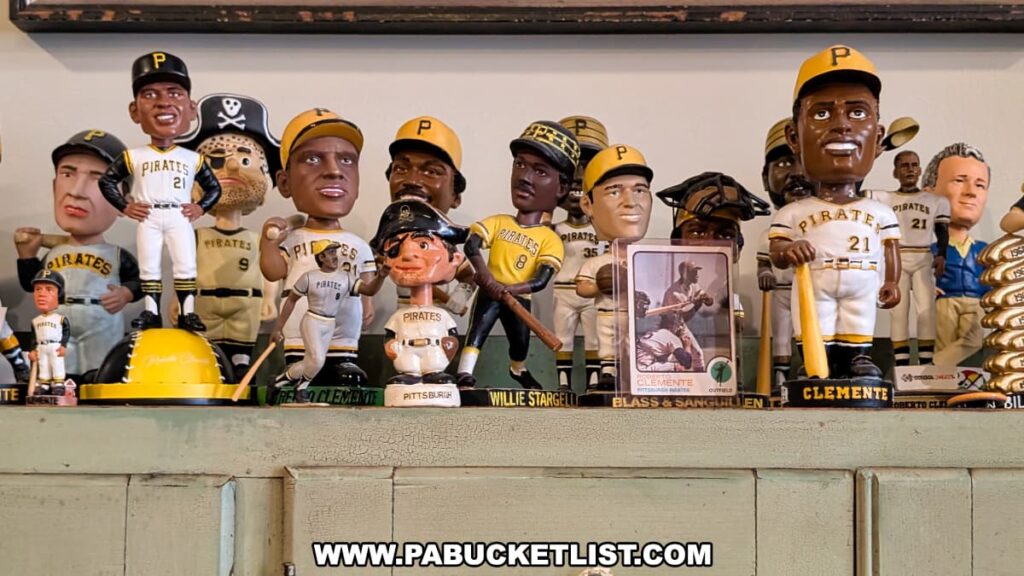 Collection of Pittsburgh Pirates bobbleheads and figurines on display at the Roberto Clemente Museum in Pittsburgh, PA, featuring multiple representations of Roberto Clemente in his number 21 jersey alongside other notable Pirates players, with a vintage Clemente baseball card prominently placed in front.