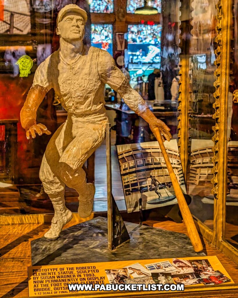 Prototype of the Roberto Clemente statue sculpted by Susan Wagner in 1993, displayed at the Roberto Clemente Museum in Pittsburgh, PA, showing Clemente in mid-stride with a bat in hand, alongside photos and information about the final statue permanently installed outside PNC Park near the Roberto Clemente Bridge.