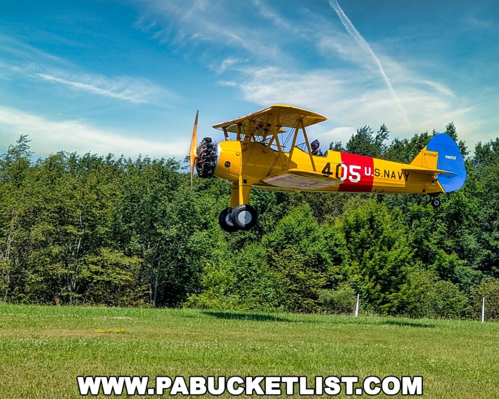 A bright yellow and blue vintage U.S. Navy biplane taking off from the grass runway at the Eagles Mere Air and Auto Museum in Sullivan County, Pennsylvania, with a pilot visible in the open cockpit, trees in the background, and a clear blue sky above, showcasing the museum’s small airport where classic aircraft take flight.