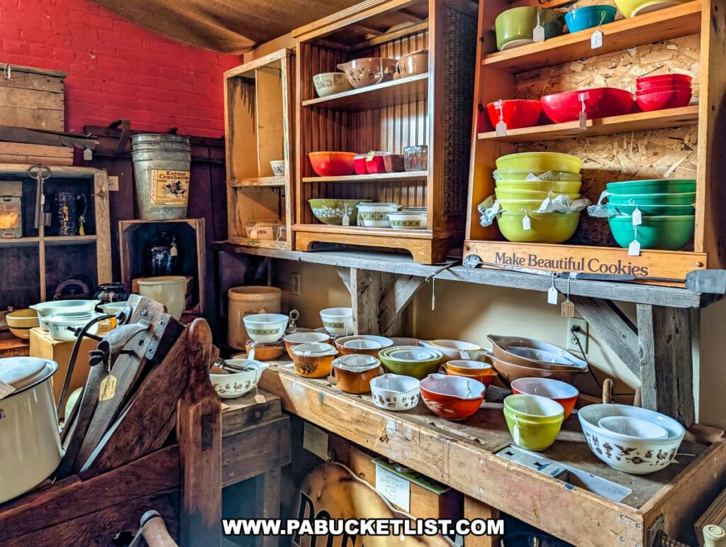 Display of vintage dishware at the Penn Avenue Trading Company in Newport, Perry County, PA, featuring colorful mixing bowls, Pyrex dishes, crockery, and rustic kitchenware arranged on wooden shelves and tables in a cozy, farmhouse-style setting with antique cabinets and decorative signage.