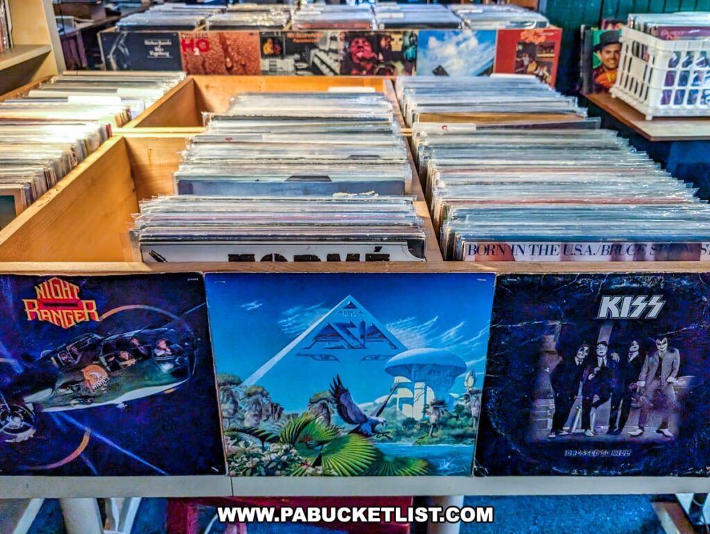 Bins of vintage vinyl records at the Penn Avenue Trading Company in Newport, Perry County, PA, with album covers for Night Ranger, Asia, and KISS prominently displayed, surrounded by rows of classic rock, pop, and country records in protective sleeves, offering a nostalgic browsing experience for music lovers.