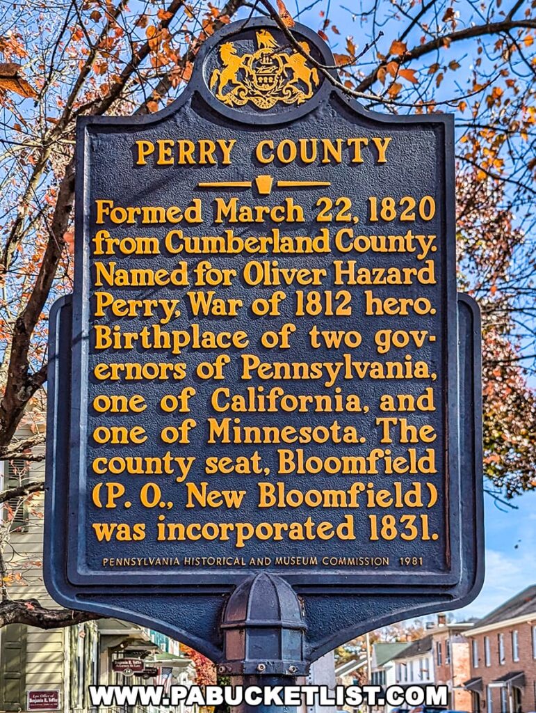 Perry County historical marker in New Bloomfield, Pennsylvania, surrounded by fall foliage and historic buildings under a bright blue sky.