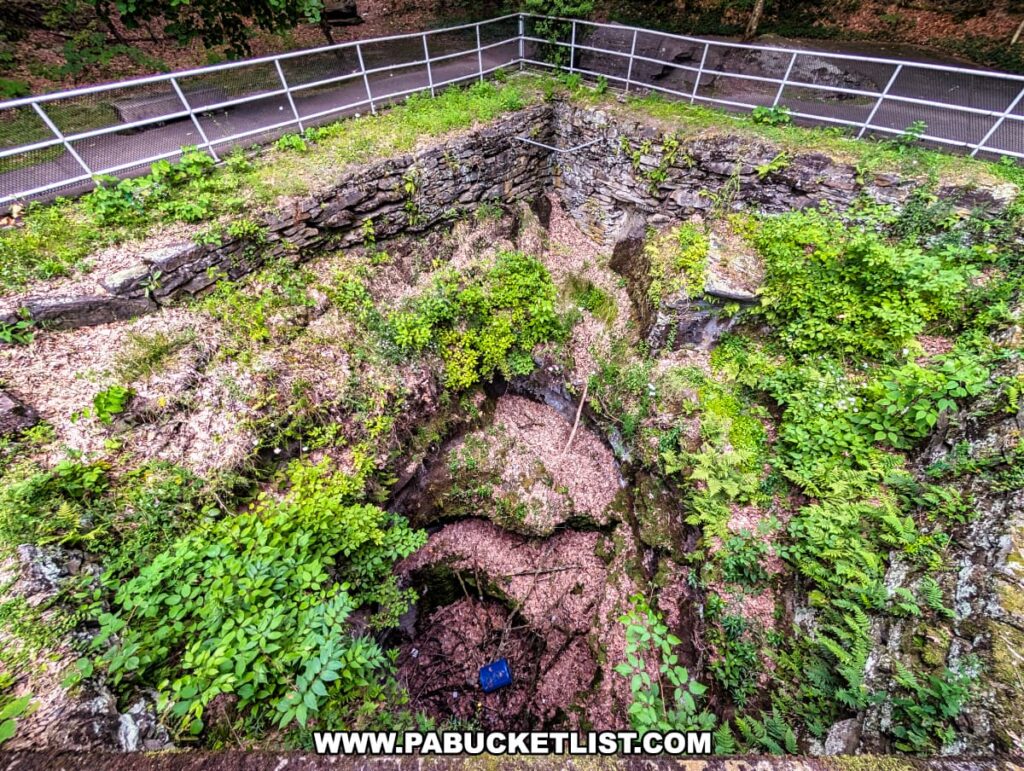 Overhead view of the enormous glacial pothole at Archbald Pothole State Park in Lackawanna County, Pennsylvania, surrounded by a stone wall, safety railings, and lush vegetation growing along the rocky edges of the 42-foot-wide natural formation.