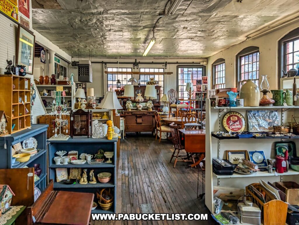 Spacious showroom at Central Station Antiques in Scranton, PA filled with vintage furniture, shelves of glassware and ceramics, decorative lamps, framed artwork, and collectibles arranged under tall windows and an industrial-style ceiling.