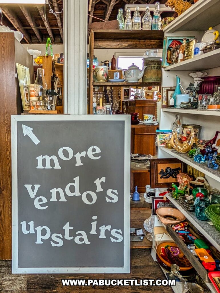 Sign inside Central Station Antiques in Scranton, PA reading “more vendors upstairs,” surrounded by shelves of vintage glassware, collectibles, and decorative items.