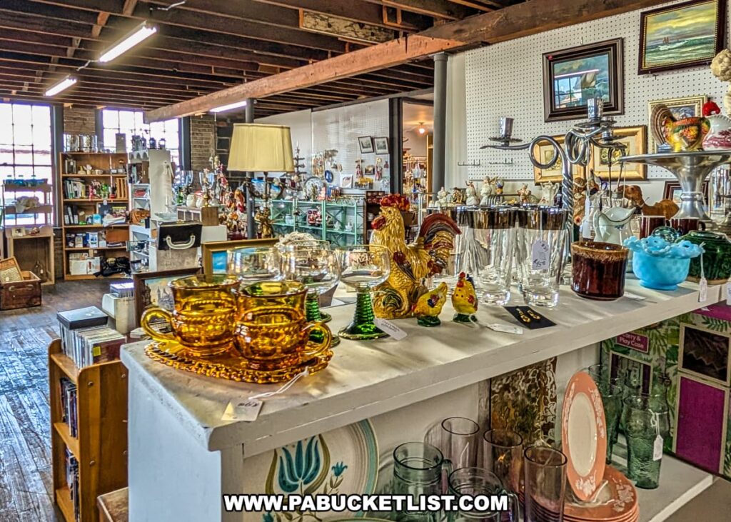 Interior view of Central Station Antiques in Scranton, PA with displays of vintage glassware, ceramic rooster figurines, framed artwork, books, and collectibles arranged on shelves and tables under exposed wooden beams.