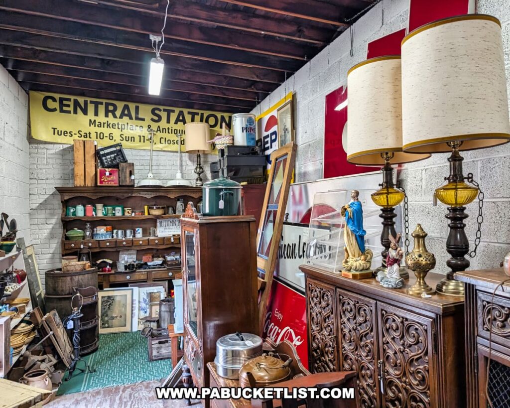 Eclectic display at Central Station Antiques in Scranton, PA featuring mid-century lamps, religious figurines, wooden furniture, vintage advertising signs, and shelves filled with kitchenware and collectibles under exposed beams.