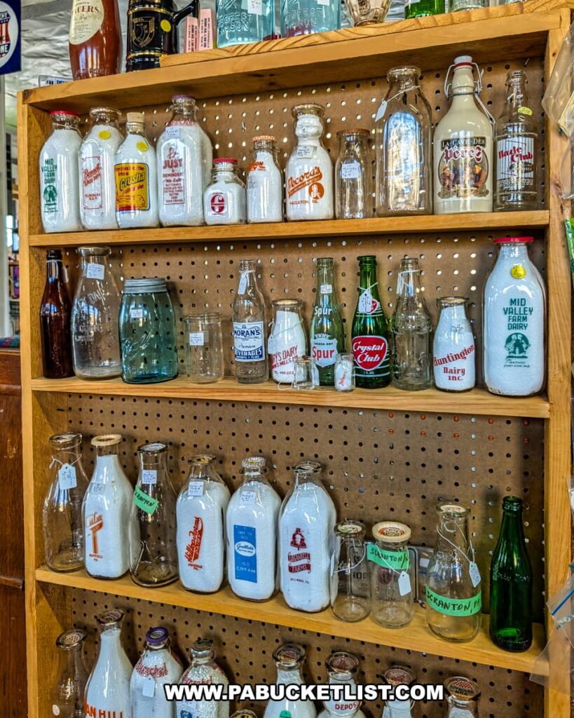 Wooden shelf display at Central Station Antiques in Scranton, PA featuring an assortment of vintage glass milk bottles, soda bottles, and dairy containers with colorful logos and lettering.