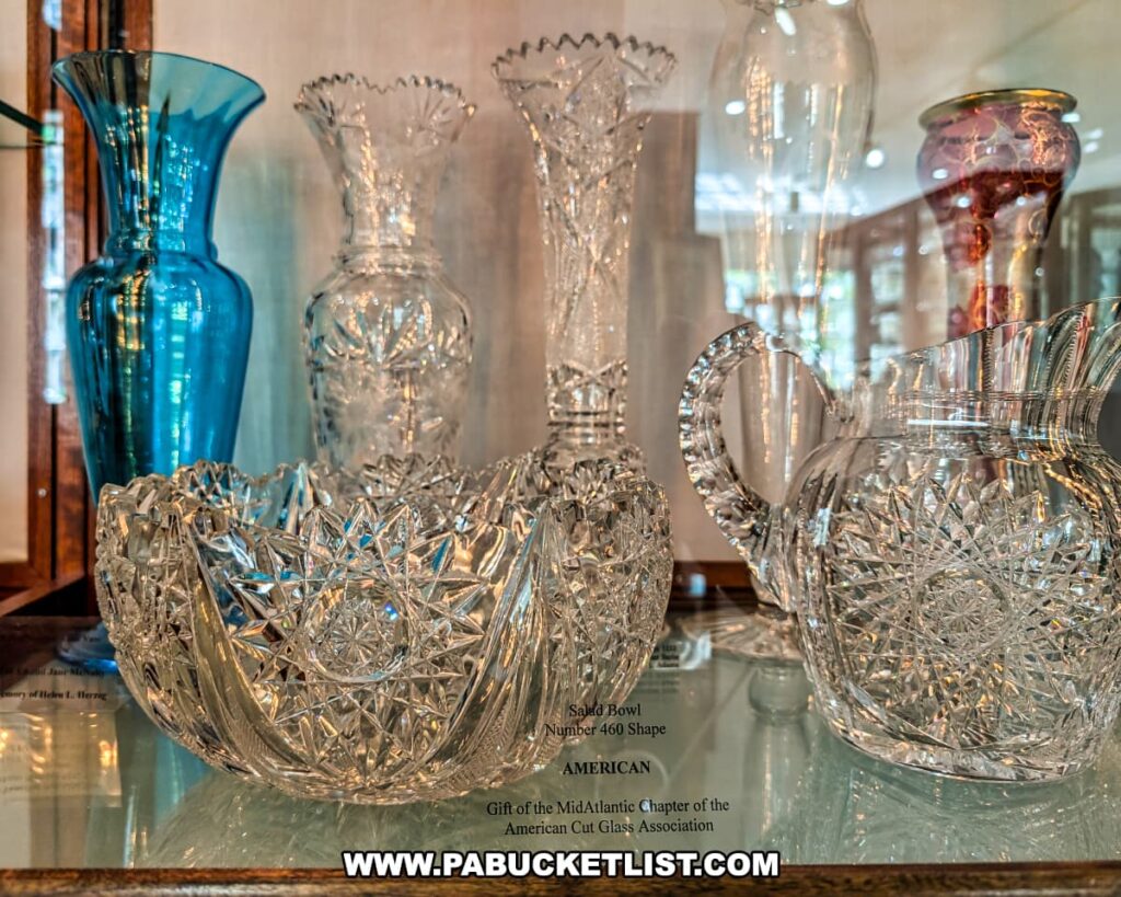 Display of intricately cut crystal pieces, including a salad bowl, pitcher, and vases, alongside colorful glassware at the Dorflinger Glass Museum in Wayne County, PA