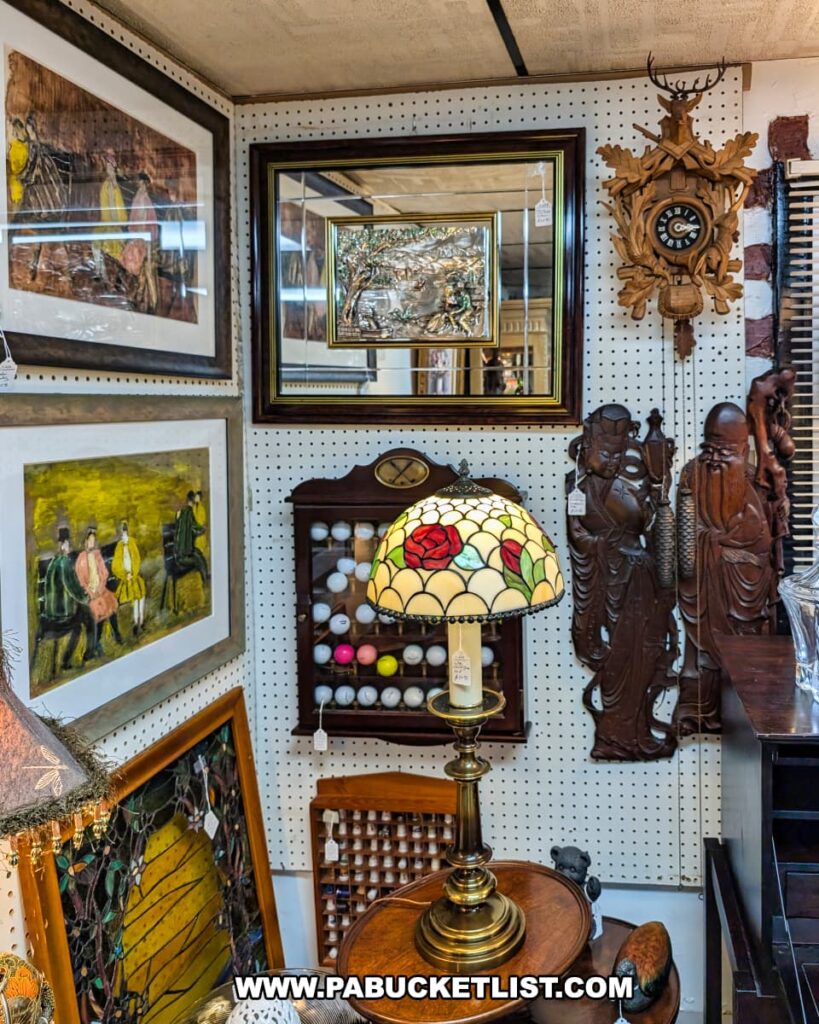 A corner display at Duchess Outlet Antiques in Luzerne County, Pennsylvania, featuring a Tiffany-style stained glass lamp with a rose design, surrounded by various antiques including a large wooden cuckoo clock, carved statues, framed artwork, and a display case filled with golf balls.