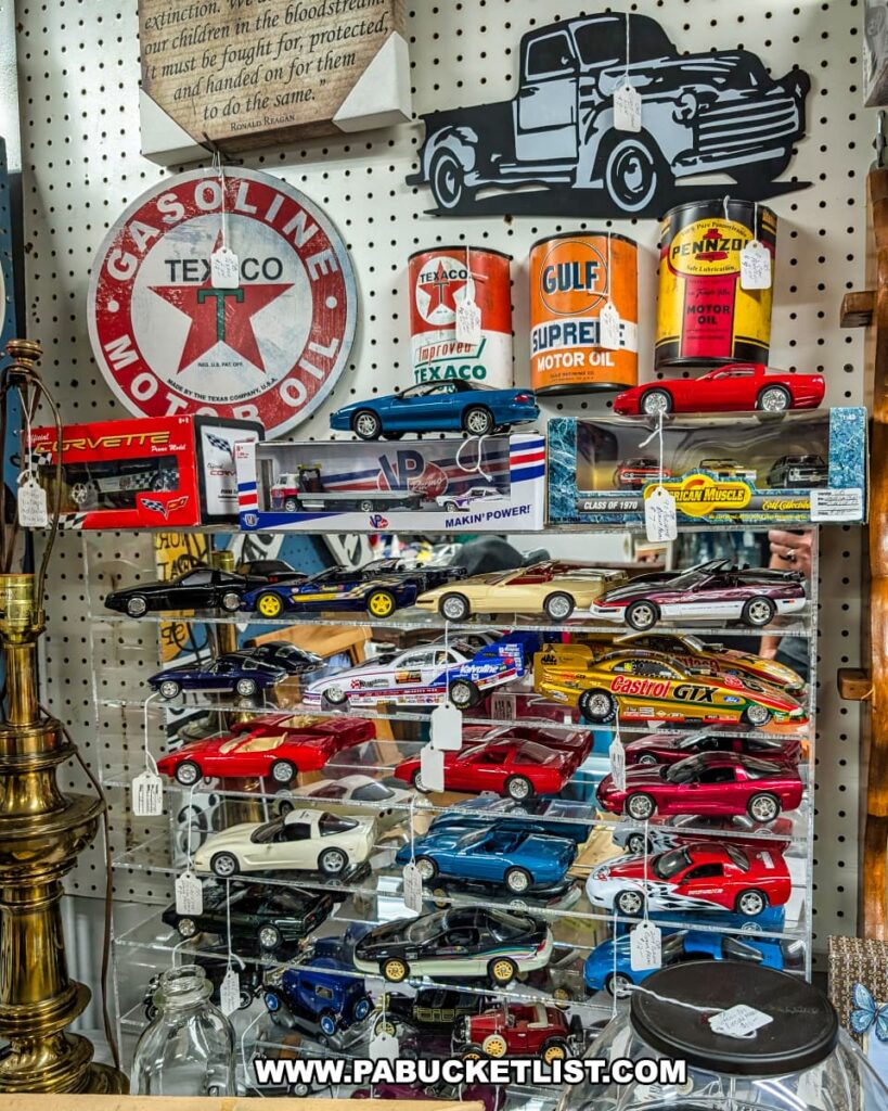 A display inside an antique store featuring a collection of vintage model cars, classic automotive advertising signs like Texaco and Gulf, old motor oil cans, and a metal art piece of a classic pickup truck, all arranged on shelves in a multi-vendor setting.