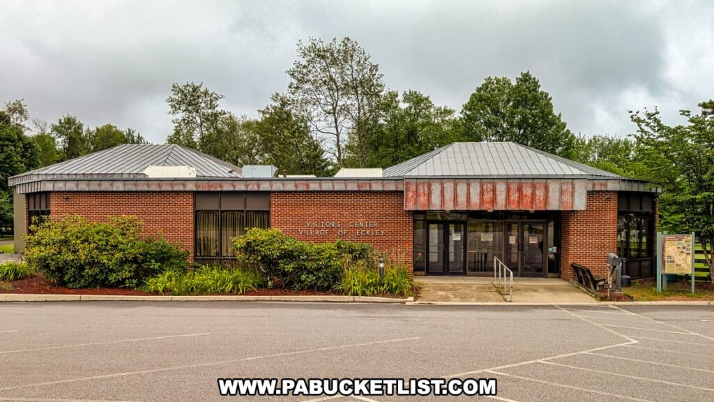 Exterior view of the Eckley Miners’ Village Visitors Center in Luzerne County, Pennsylvania, a brick building with a metal roof surrounded by greenery, serving as the museum entrance and starting point for exploring the historic coal mining town.