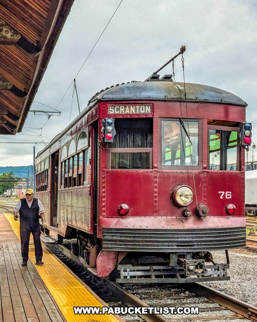 A vintage maroon trolley marked “Scranton” sits at the platform during the Electric City Trolley Museum’s 5.5 mile round-trip excursion in Lackawanna County, with a uniformed crew member standing alongside.
