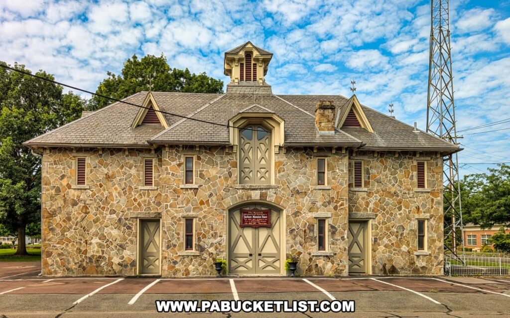 Historic stone carriage house at the Jackson Mansion in Berwick, Pennsylvania, featuring symmetrical architecture, dormer windows, and a central cupola beneath a partly cloudy sky.