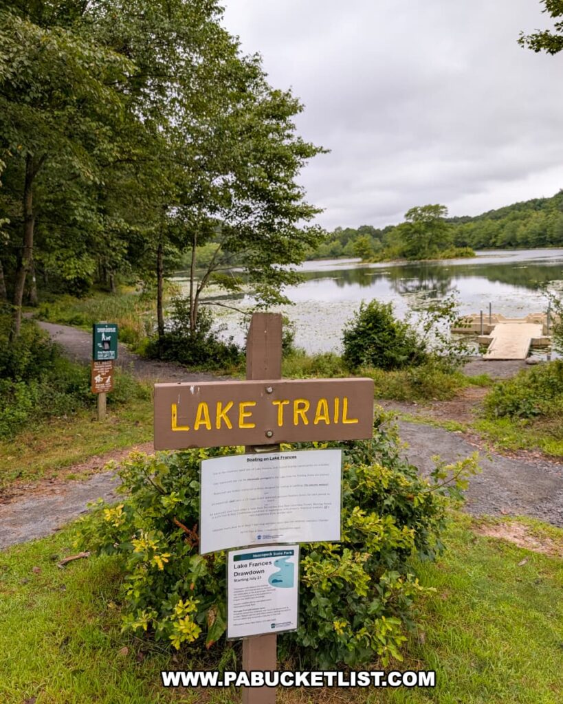 Lake Trail sign at Nescopeck State Park in Luzerne County with Lake Frances, a boat launch, and surrounding forest visible in the background.