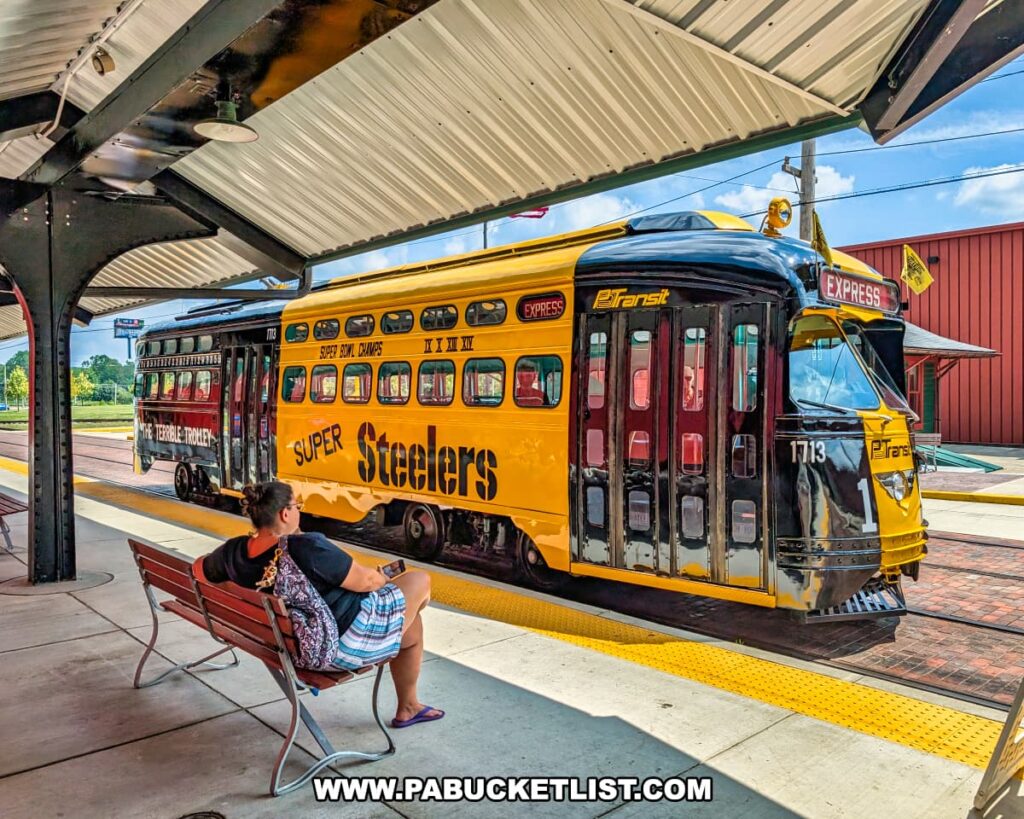Pittsburgh Steelers–themed trolley known as “The Terrible Trolley” painted in black and gold at the Pennsylvania Trolley Museum in Washington County, Pennsylvania, with a visitor seated on a bench at the station platform.